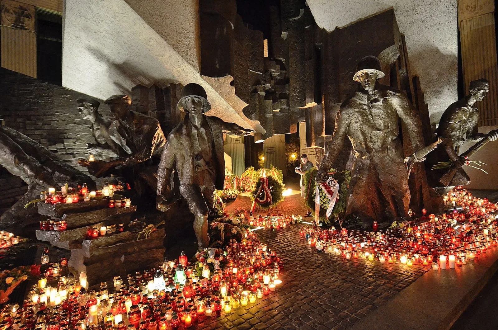 A night landscape of a war memorial with statues and many lit candles in front of them, illuminating the scene.